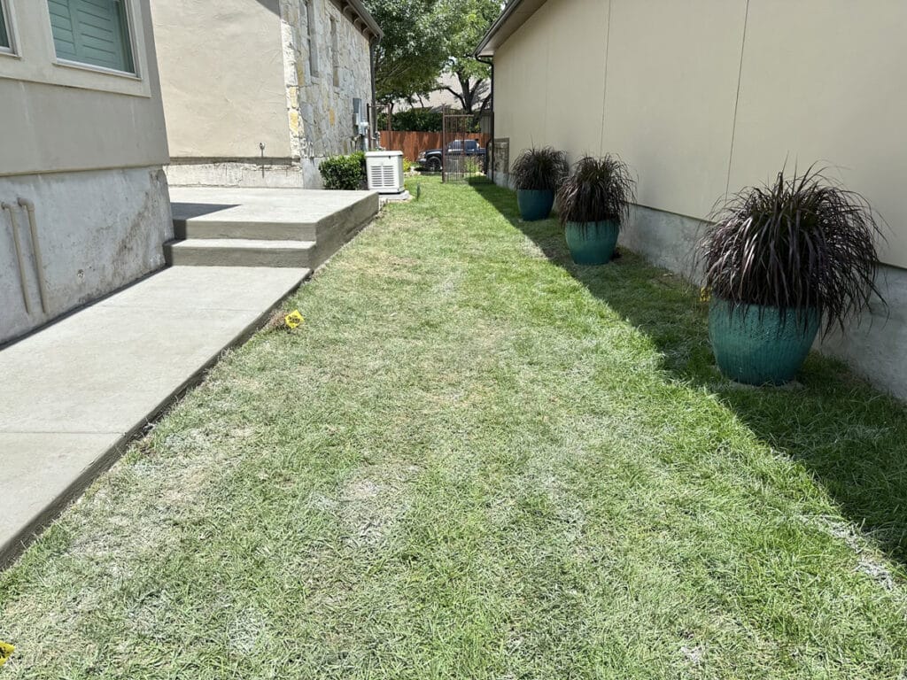 A newly laid concrete sidewalk running alongside a house with decorative potted plants and a well-maintained lawn in San Antonio.