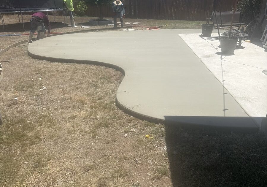 Construction team working on a new, winding concrete patio in the backyard of a residential home on a sunny day.
