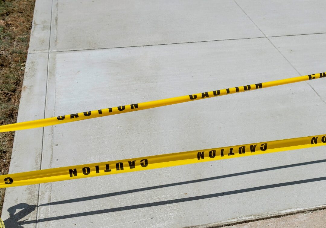 New concrete sidewalk section cordoned off with bright yellow caution tape to prevent walking on the fresh surface.